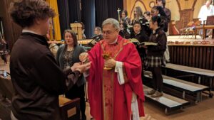 Bishop Schlert giving Communion to a Bethlehem Catholic Student during the Catholic Schools' Week Mass. Mrs. Maigur is to the left of Bishop Schlert, the choir is behind him singing the communion hymn